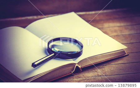 Loupa and book on wooden table 13879895