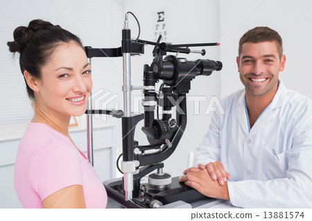Happy optician and female patient with slit lamp Happy optician and female patient with slit lamp 13881574