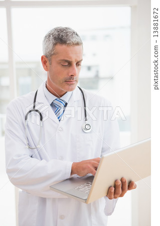 Doctor using laptop smiling to camera Doctor using laptop smiling to camera 13881672