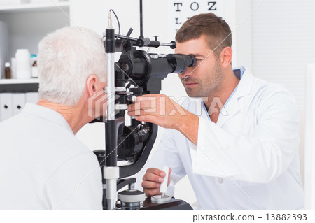 Optometrist examining senior mans eyes through slit lamp 13882393