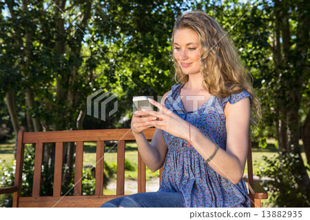 Pretty blonde using phone in the park 13882935