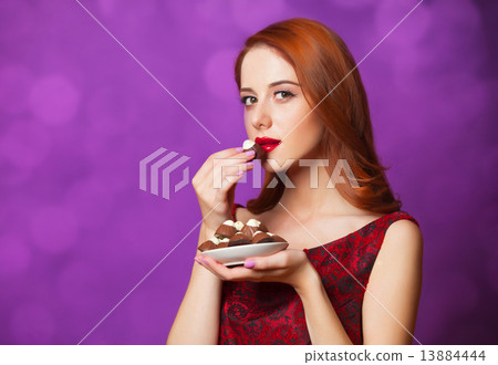 Redhead women with candy on violet background. 13884444