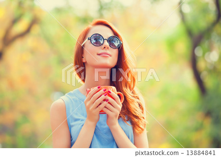 Successful redhead girl winh cup in the autumn park. Successful redhead girl winh cup in the autumn park. 13884841