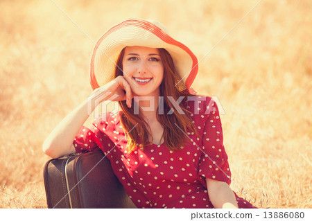 Redhead girl with suitcase sitting at grass 13886080