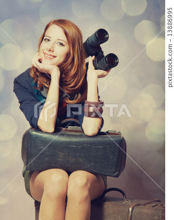 Redhead girl with binocular sitting on the big suitcase 13886995