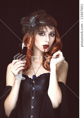 Redhead vampire woman with glass of blood. Photo in vintage styl 13887601
