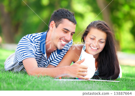 Young students sitting on green grass with note book. 13887664