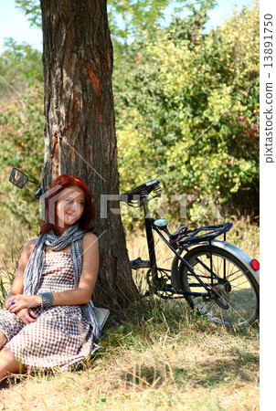 Beautiful girl sitting near bike and tree at rest in forest. Beautiful girl sitting near bike and tree at rest in forest. 13891750