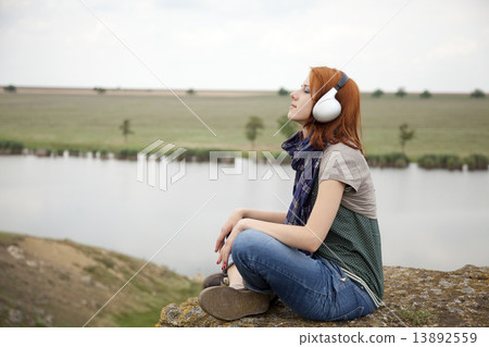 Young fashion girl with headphones at rock near lake. 13892559