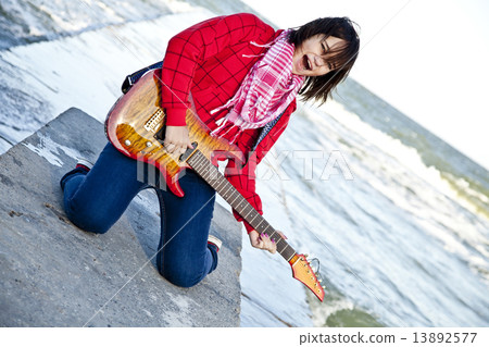 Young brunet girl play on guitar at sea pier in wind day. 13892577