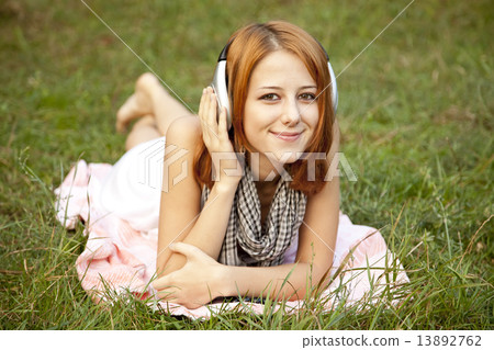 Young fashion girl with headphone lying at green grass 13892762