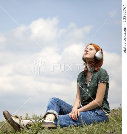 Young smiling girl with headphones sitting at green grasss. Young smiling girl with headphones sitting at green grasss. 13892764