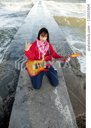 Young brunet girl play on guitar at sea pier in wind day. 13892804