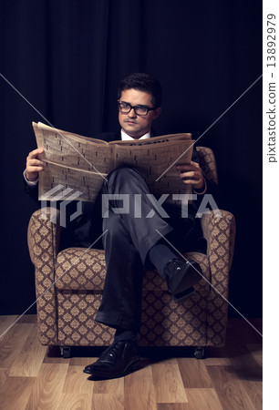 Man with cigarette and newspaper sitting in vintage armchair 13892979