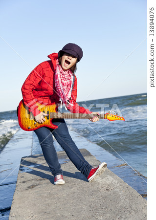 Young brunet girl play on guitar at sea pier in wind day. 13894076