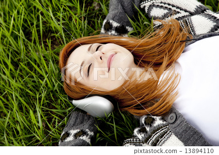 Young fashion girl with headphones lying at green spring grass. 13894110