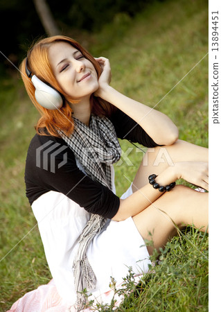 Young fashion girl with headphone sitting at green grass 13894451