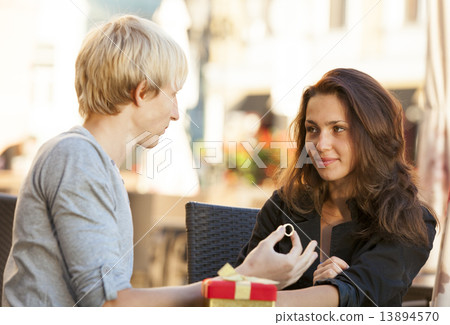 The young man gives a gift to a young girl in the cafe 13894570