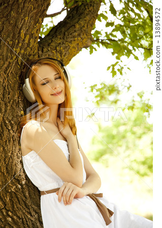 Beautiful redhead girl with headphones at garden. Beautiful redhead girl with headphones at garden. 13894572
