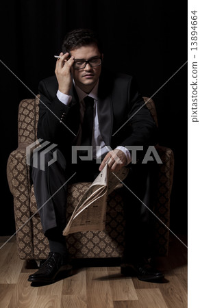 Man with cigarette and newspaper sitting in vintage armchair 13894664