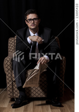 Man with cigarette and newspaper sitting in vintage armchair Man with cigarette and newspaper sitting in vintage armchair 13895410