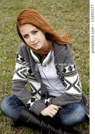 Sad girl with headphones sitting at green spring grass. Sad girl with headphones sitting at green spring grass. 13895577