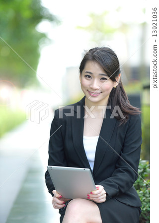 One young successful Chinese businesswoman holding tablet iPad sitting along promenade 13921036