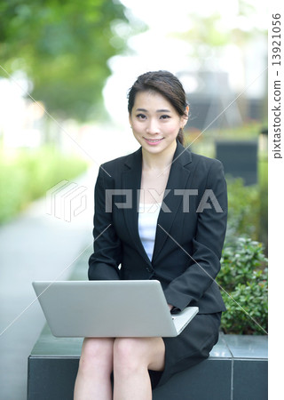 One young successful Chinese businesswoman using laptop sitting along promenade 13921056