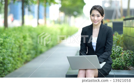 One young successful Chinese businesswoman using laptop sitting along promenade One young successful Chinese businesswoman using laptop sitting along promenade 13921058