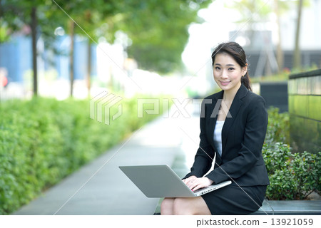 One young successful Chinese businesswoman using laptop sitting along promenade One young successful Chinese businesswoman using laptop sitting along promenade 13921059