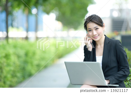 One young successful Chinese businesswoman using mobile phone and laptop sitting along promenade 13921117