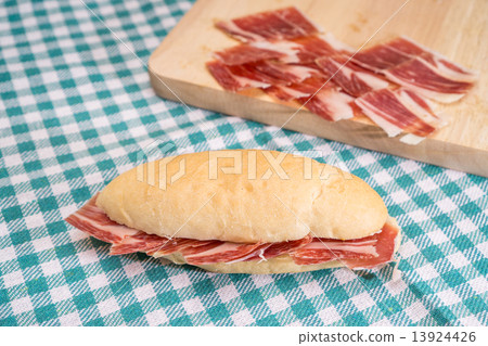 Side view of Serrano ham sandwich over checkered tablecloth 13924426