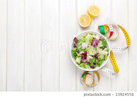Fresh healthy salad, utensils and tape measure over white wooden Fresh healthy salad, utensils and tape measure over white wooden 13924558