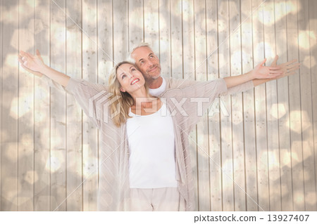 Composite image of happy couple standing with arms outstretched 13927407
