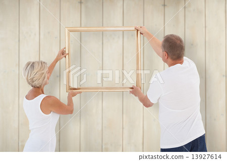 Composite image of mature couple hanging up picture frame Composite image of mature couple hanging up picture frame 13927614