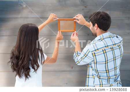 Composite image of happy young couple putting up picture frame Composite image of happy young couple putting up picture frame 13928088