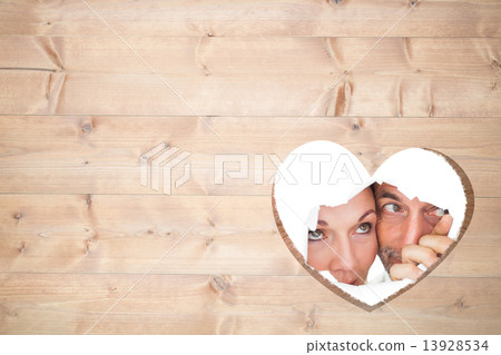 Composite image of couple looking through torn paper Composite image of couple looking through torn paper 13928534