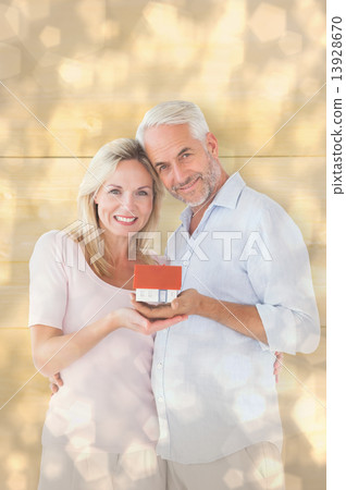 Composite image of happy couple holding miniature model house Composite image of happy couple holding miniature model house 13928670