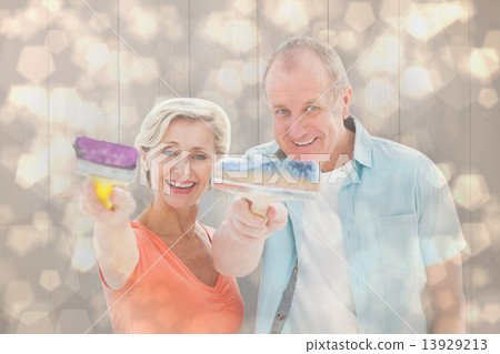 Composite image of happy older couple holding paintbrushes Composite image of happy older couple holding paintbrushes 13929213