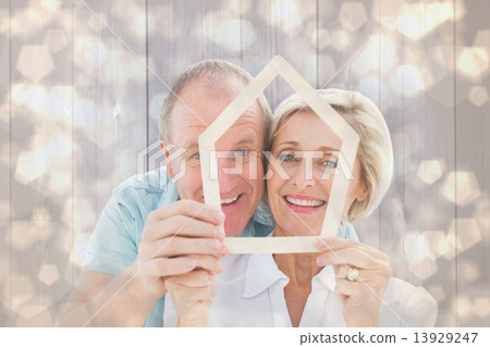 Composite image of happy older couple holding house shape 13929247