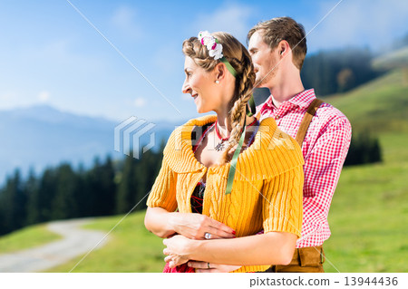 Couple in Tracht on Alp mountain summit at vacation 13944436