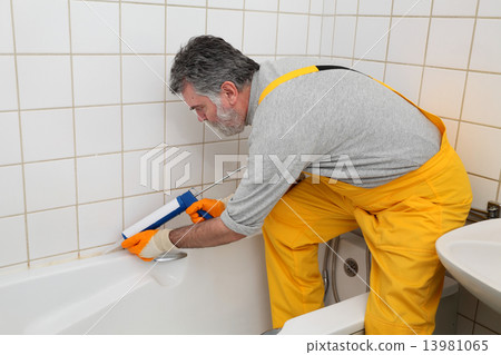 Worker caulking bath tube and tiles 13981065