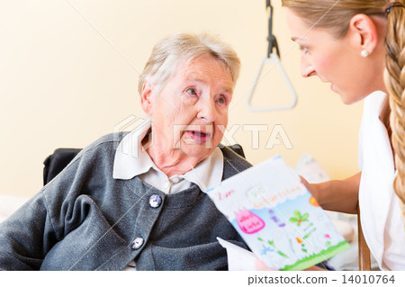 Nurse giving birthday card to senior woman in home Nurse giving birthday card to senior woman in home 14010764