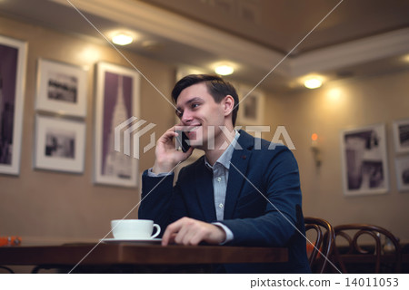 Young businessman on the phone with a smile his face and cup of cofee front him Young businessman on the phone with a smile his face and cup of cofee front him 14011053