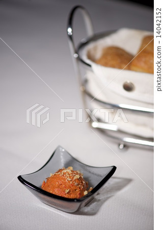 Dish of orange paste beside bread basket Dish of orange paste beside bread basket 14042152