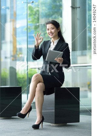 Successful chinese businesswoman giving ok gesture using tablet iPad sitting along promenade Successful chinese businesswoman giving ok gesture using tablet iPad sitting along promenade 14049247