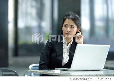 Chinese businesswoman in thoughts while using laptop along office promenade 14049363
