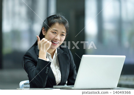 Chinese businesswoman giving thumbs up while using laptop along office promenade 14049366