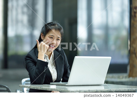 Chinese businesswoman giving thumbs up while using laptop along office promenade 14049367