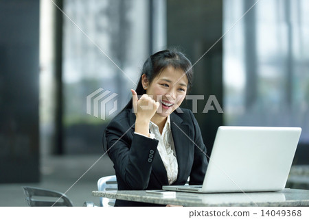 Chinese businesswoman giving thumbs up while using laptop along office promenade 14049368